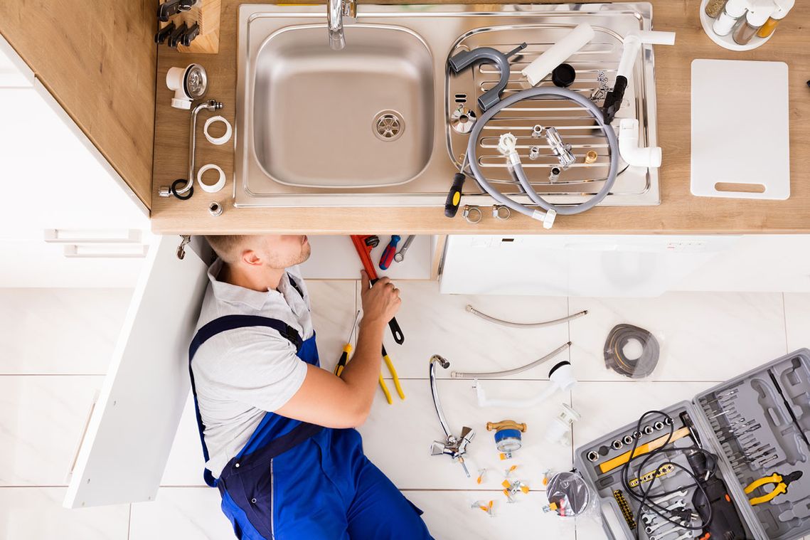 A plumber making repairs under a kitchen sink